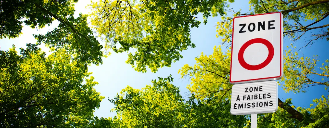 Panneau de zone à faibles émissions (ZFE) sur fond de feuillage vert et ciel ensoleillé